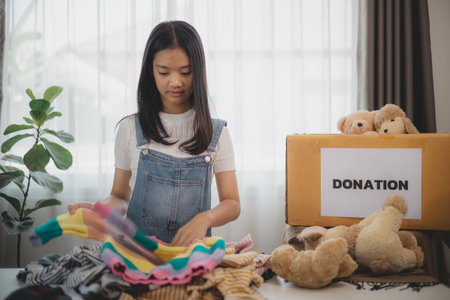 Recycling, Donation, Asian girls packing objects at home, putting on stuff into donate box with second hand clothes, charity helping and people. Reuse recycle, moving.の写真素材