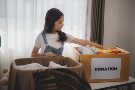 Recycling, Donation, Asian girls packing objects at home, putting on stuff into donate box with second hand clothes, charity helping needy people. Reuse recycle, moving.の写真素材