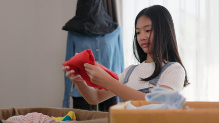 Recycling, Donation for poor, Asian girls packing objects at home, putting on stuff into donate box with second hand clothes, charity helping and needy people. Reuse recycle, moving.の写真素材