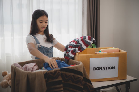 Recycling, Donation for poor, Asian girls packing objects at home, putting on stuff into donate box with second hand clothes, charity helping and needy people. Reuse recycle, moving.の写真素材