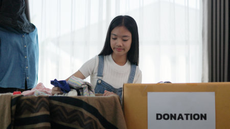 Recycling, donation, Asian girls packing objects at home, putting on stuff into donate box with second hand clothes, charity helping people. Reuse recycle, moving.の写真素材