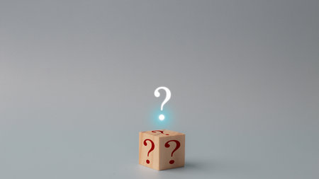 A wooden cube with a red question mark on it is on a yellow background. The cube is placed in the center of the image, and the question mark is pointing upwards. Concept of curiosity and intrigueの写真素材