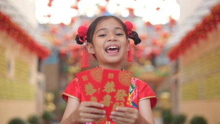 Asian girl wearing red traditional Chinese cheongsam decoration holding red envelopes in hand and lanterns with the Chinese text Blessings written on it Is a Fortune blessing for Chinese New Yearの写真素材