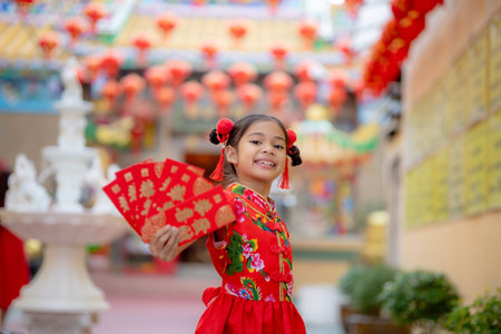 Asian girl wearing red traditional Chinese cheongsam decoration holding red envelopes in hand and lanterns with the Chinese text Blessings written on it Is a Fortune blessing for Chinese New Yearの写真素材