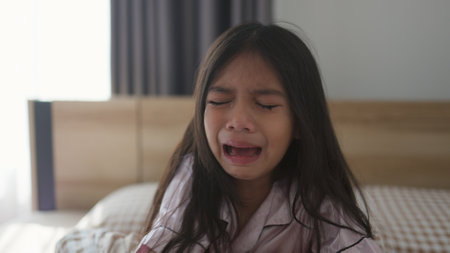 The scared little girl in the bedroom crying with her hands holding her teddy in fear of monsters in darkness in the bedroom in the Child's nightmares imagination and psychological distress concept.の写真素材
