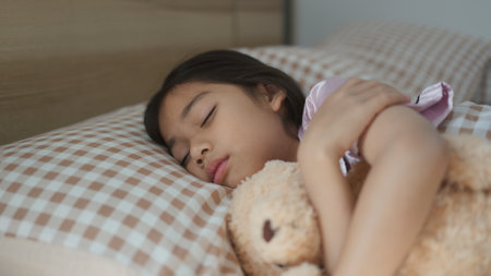 Cute Asian little girl sleeping with teddy bear in bedの写真素材
