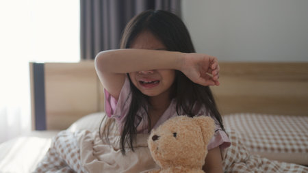 The scared little girl in the bedroom crying with her hands holding her teddy in fear of monsters in darkness in the bedroom in the Child's nightmares imagination and psychological distress concept.の写真素材