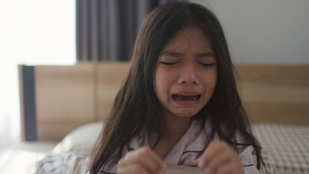 The scared little girl in the bedroom crying with her hands holding her teddy in fear of monsters in darkness in the bedroom in the Child's nightmares imagination and psychological distress concept.の写真素材