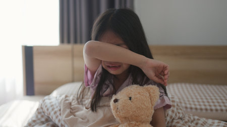 The scared little girl in the bedroom crying with her hands holding her teddy in fear of monsters in darkness in the bedroom in the Child's nightmares imagination and psychological distress concept.の写真素材