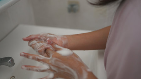 Little girl washing hands with water and soap in the bathroom. Happy kid showing soapy palms. Hands hygiene and virus infection prevention.の写真素材