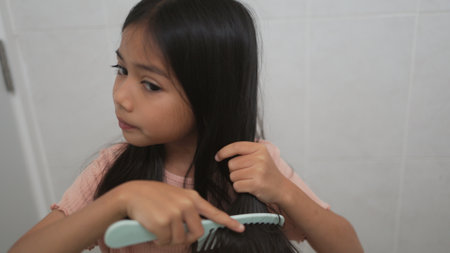 Little Asian girl combing hair in the bathroom, caring for a child's hairの写真素材