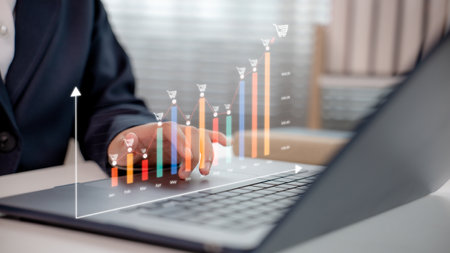 Businessman using laptop with rising monthly ecommerce sales chart and shopping cart icons, representing revenue growth, digital business analytics, and online retail strategy.の写真素材