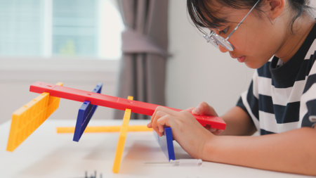 Asian girl learning STEM by assembling mechanical parts with focus and determination. Concept of hands-on education, child engineering, creativity, and science learning at home.の写真素材