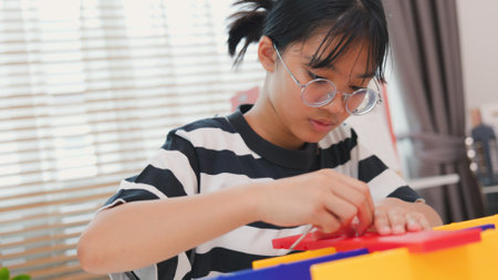 Asian girl learning STEM by assembling mechanical parts with focus and determination. Concept of hands-on education, child engineering, creativity, and science learning at home.の写真素材