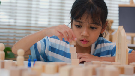 Young Asian girl focused on stacking wooden blocks, promoting STEM learning, creativity, and motor skill development. Concept of early education, problem solving, and cognitive growth.の写真素材