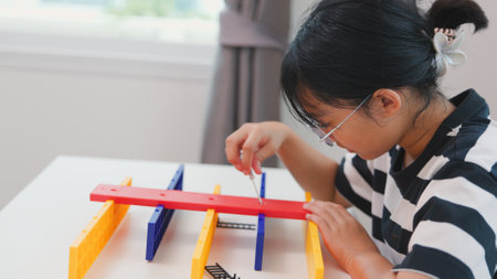 Asian girl assembling a colorful plastic structure with a screwdriver as part of a STEM learning activity. Concept of hands-on education, child engineering, creativity, and problem solving.の写真素材