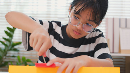 Asian girl learning STEM by assembling mechanical parts with focus and determination. Concept of hands-on education, child engineering, creativity, and science learning at home.の写真素材