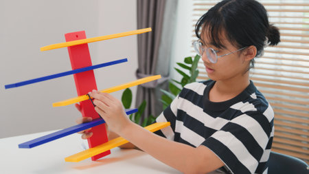 Asian girl learning STEM by assembling mechanical parts with focus and determination. Concept of hands-on education, child engineering, creativity, and science learning at home.の写真素材