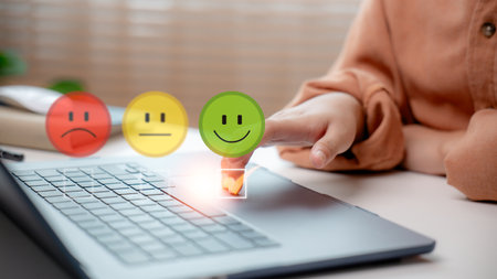 The user hand selected a happy smiley face on the virtual satisfaction survey over the laptop, representing customer feedback, rating, experience evaluation, and positive service review.の写真素材