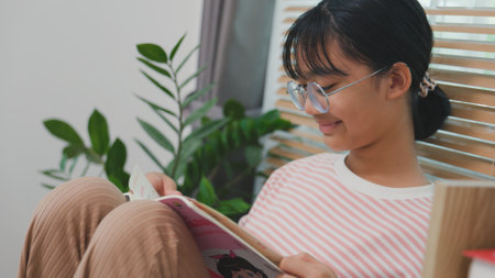 Teen girl reading a book at home with concentration. Concept of self-learning, education, student lifestyle, and knowledge development in a calm, cozy environment.の写真素材