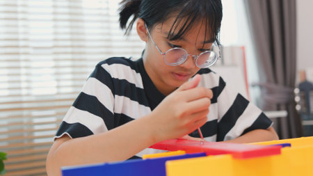 Asian girl learning STEM by assembling mechanical parts with focus and determination. Concept of hands-on education, child engineering, creativity, and science learning at home.の写真素材