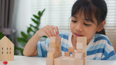 Young Asian girl focused on stacking wooden blocks, promoting STEM learning, creativity, and motor skill development. Concept of early education, problem solving, and cognitive growth.の写真素材