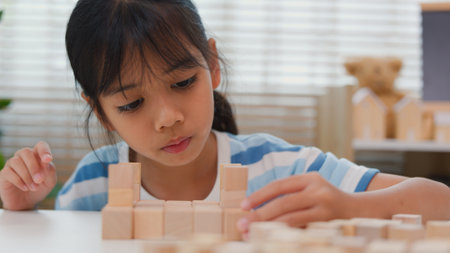 Young Asian girl focused on stacking wooden blocks, promoting STEM learning, creativity, and motor skill development. Concept of early education, problem solving, and cognitive growth.の写真素材