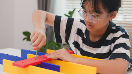Asian girl assembling a colorful plastic structure with a screwdriver as part of a STEM learning activity. Concept of hands-on education, child engineering, creativity, and problem solving.の写真素材