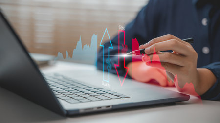Hand holding a pen analyzing cost reduction and quality improvement chart on a laptop, symbolizing business strategy, performance optimization, ROI, and effective financial planning.の写真素材
