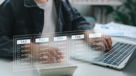 Close-up of person using calculator and laptop with digital tax forms on screen. Concept of online tax filing, financial technology, e-filing system, accounting software, and tax automation.の写真素材