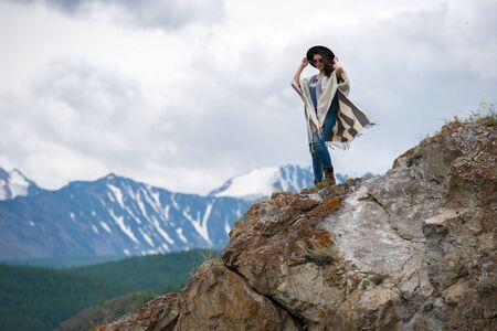 beautiful girl in a hat and sunglasses standing on the edge of the cliff and clings to a hatの写真素材