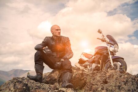 Bald rider sits on a mountain next to a motorcycle and looks asideの写真素材