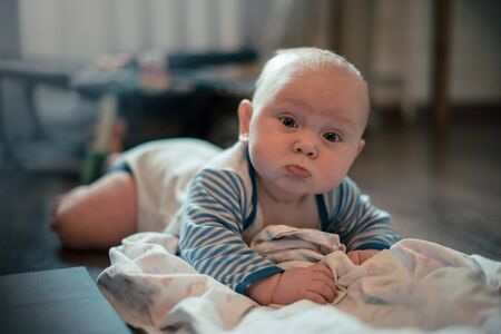 sullen child is lying on the wooden floor and playing with a diaperの写真素材