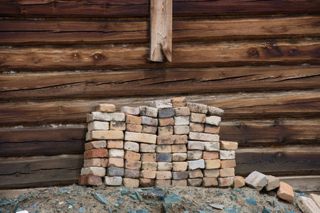 Pile of old bricks on the background wall of a wooden house. Russia.