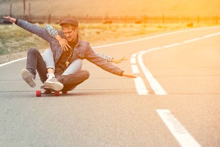 The guy with the girl drive to longboard on a mountain road. Woman hugging man. Their hands separated in different directionsの写真素材