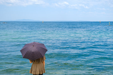 Woman with umbrella on the beach. Sea and blue sky background.の写真素材