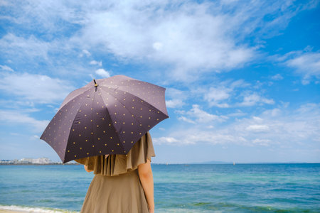 Woman with umbrella standing on the beach and looking at the sea.の写真素材