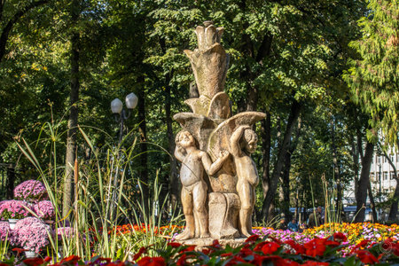 statuettes representing children in the form of an artesian fountain, in the park, surrounded by multicolored flowers and trees, autumnの写真素材
