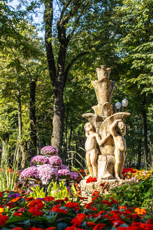 statuettes representing children in the form of an artesian fountain, in the park, surrounded by multicolored flowers and trees, autumnの写真素材