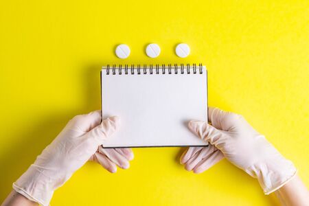 Hands with notepad for notes in rubber gloves on a yellow backgroundの写真素材