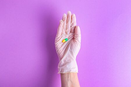 Pills in hand in a rubber glove therapy of a disease of a person on a purple backgroundの写真素材
