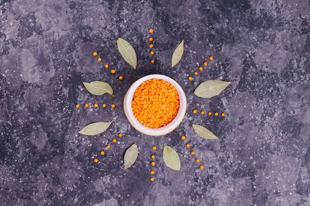 Orange raw lentils for proper nutrition and health in a white plate with bay leaf and sunbeams on a gray backgroundの写真素材