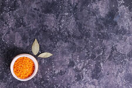 Orange raw lentils for proper nutrition and health in a white plate with bay leaf on a gray backgroundの写真素材