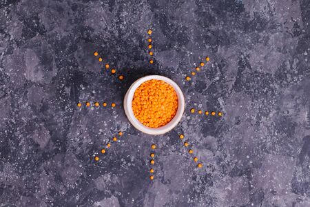 Orange raw lentils for proper nutrition and health in a white plate with sunbeams on a gray backgroundの写真素材