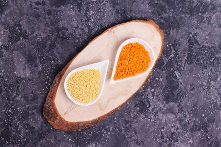 Raw orange lentils and yellow millet for proper nutrition and health in white plates on a wooden stand on a gray backgroundの写真素材