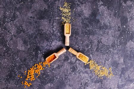 Raw orange lentils, millet and bulgur for proper nutrition and health in wooden spoons on a gray backgroundの写真素材