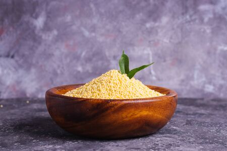 Raw yellow millet for proper nutrition and health in a wooden plate on a gray backgroundの写真素材