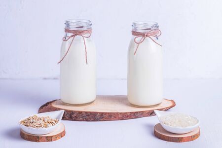 Rice and oat vegan milk in glass bottles on a wooden stand on a white backgroundの写真素材