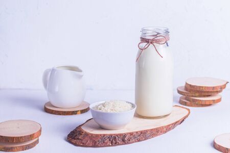 Vegan rice milk in a glass bottle and rice in a white plate on a wooden stand on a white backgroundの写真素材