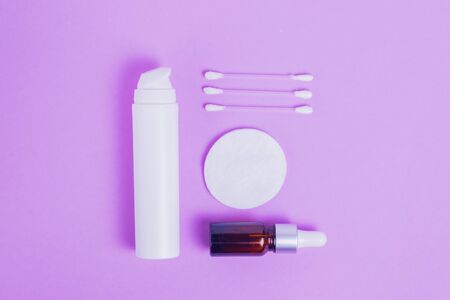 Moisturizing face cream with collagen and mucin of a snail for the skin of the face against wrinkles and acne in a white packaging with a pump and face serum in a glass bottle with makeup sticks and cotton pads on a purple backgroundの写真素材